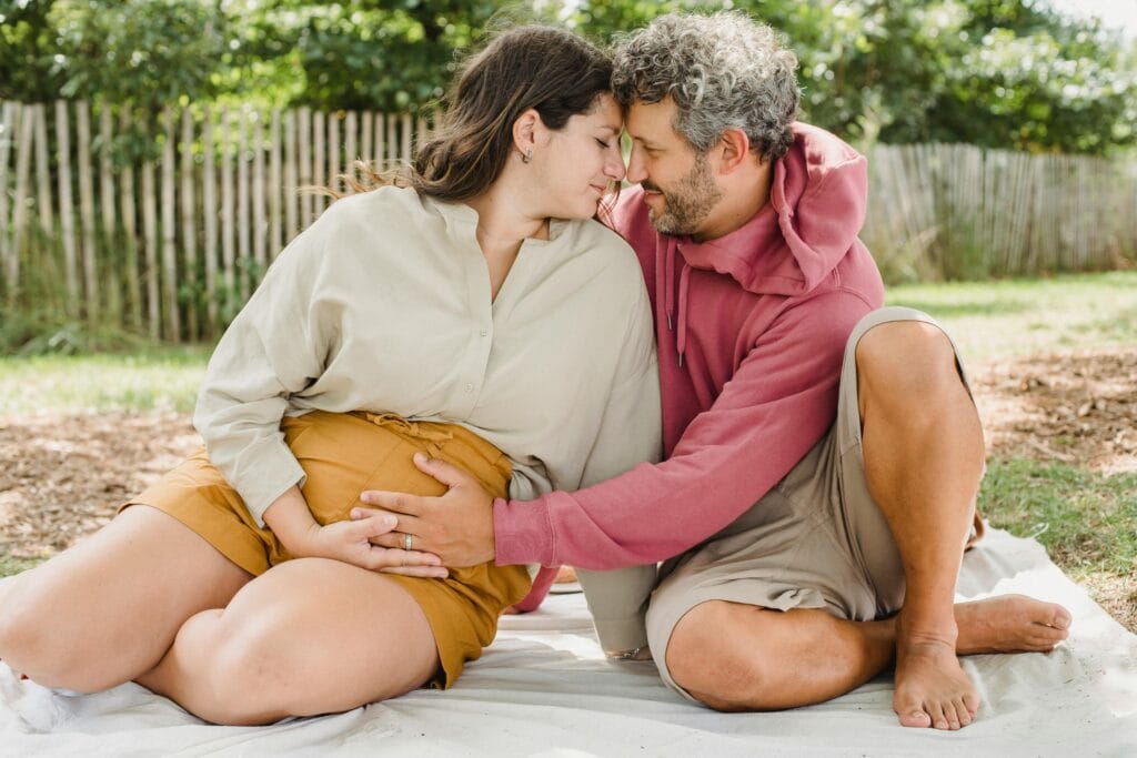 A man and his pregnant partner sitting outdoors in an intimate pose