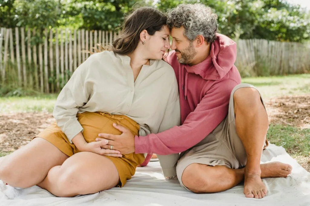 A man and his pregnant partner sitting outdoors in an intimate pose